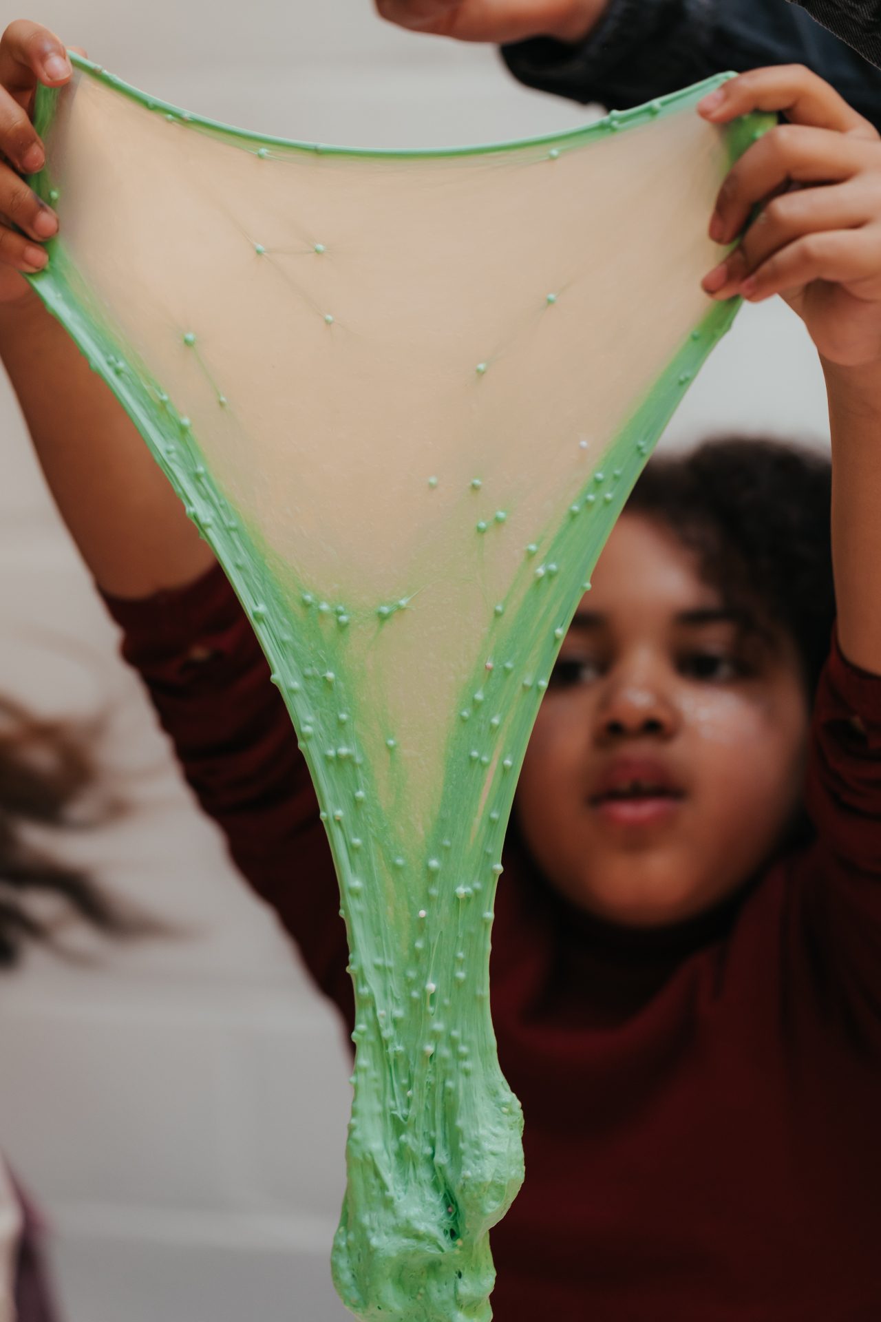Atelier Slime Art Studio — enfant étirant une slime verte pastel garnie de perles crunchy en forme de voile translucide