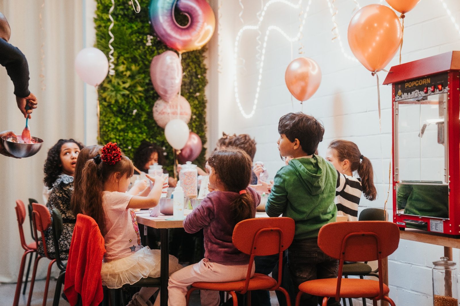 Atelier slime à Mons — enfants en pleine création avec ballons roses, mur végétal et machine à pop-corn